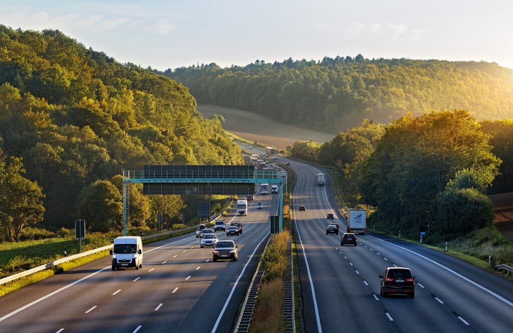 Flotte de véhicules circulant sur une autoroute traversant une zone boisée, illustrant les enjeux de mobilité et de gestion des risques routiers en entreprise.