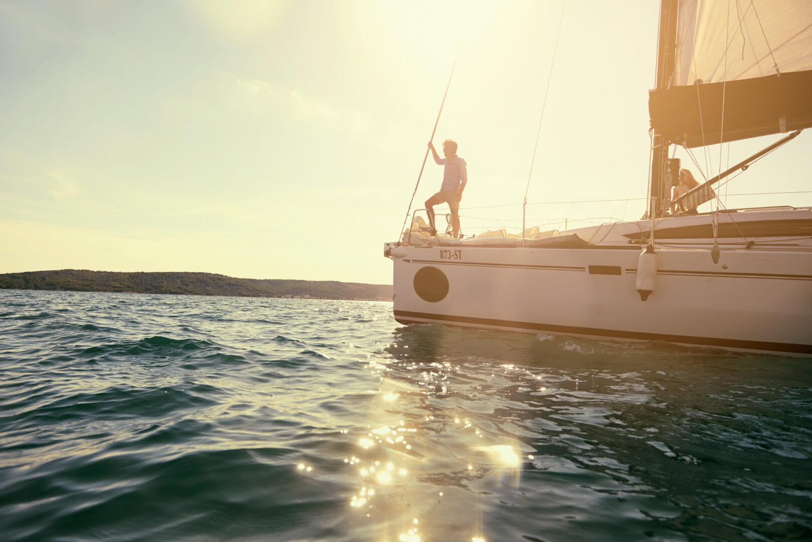 Personne debout à l’avant d’un voilier naviguant sous le soleil.