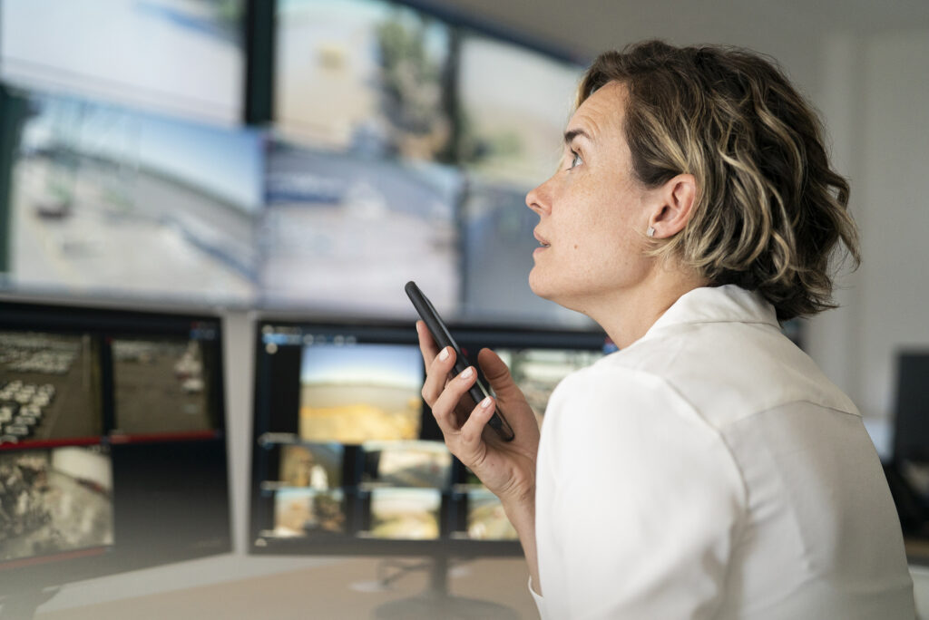 Centre de supervision avec écrans de contrôle affichant des flux de vidéosurveillance et dispositif de communication mobile.