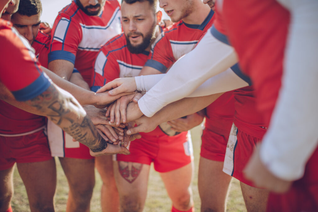 Joueurs d’une équipe sportive réunissant leurs mains avant une compétition, symbole de cohésion et de solidarité.