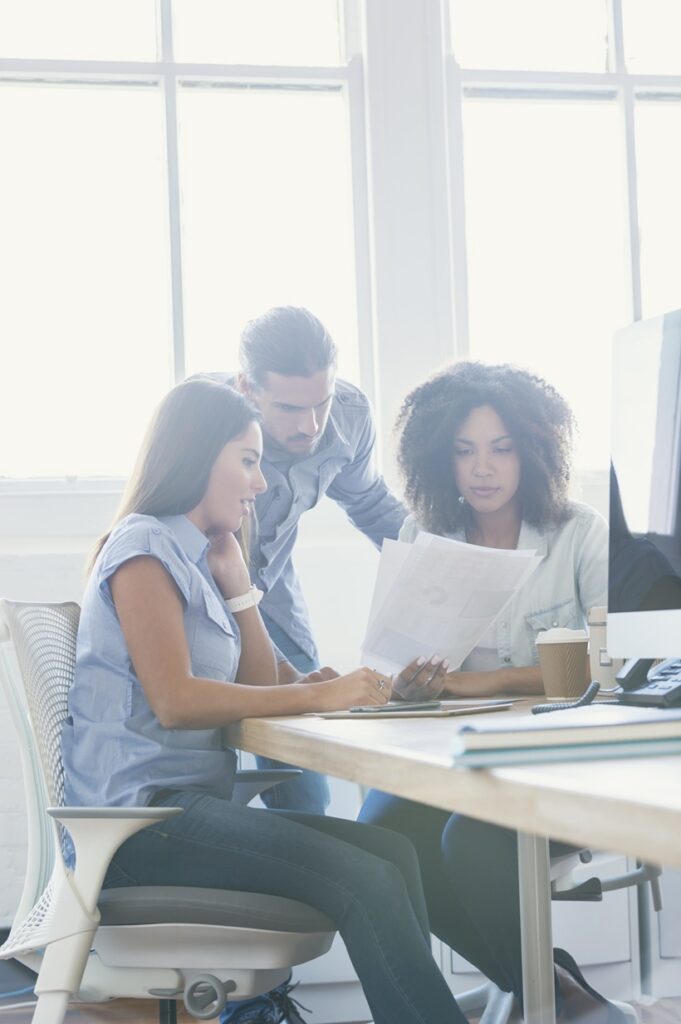 Réunion de travail autour de documents et d’un poste informatique dans un environnement de bureau moderne.