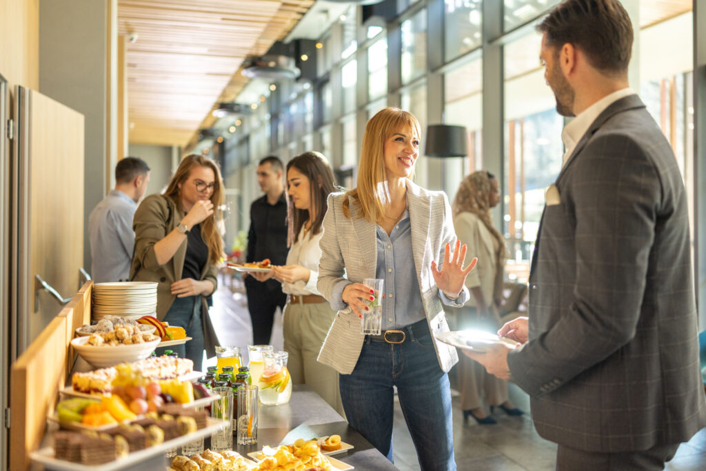 Participants échangeant lors d’un séminaire professionnel autour d’un espace de restauration dans un lieu moderne.
