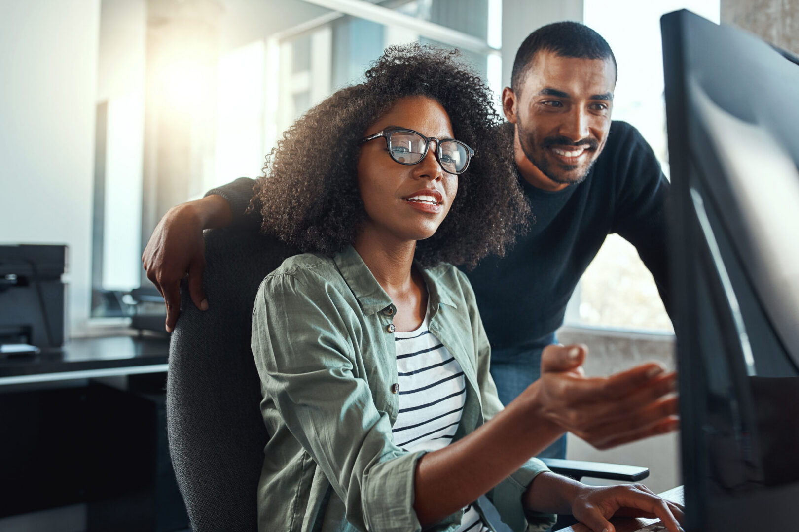 Deux collaborateurs échangeant autour d’un écran dans un environnement de travail moderne.