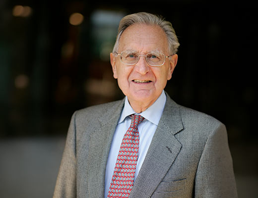 Portrait professionnel d’une personne en costume, photographiée sur fond sombre et flou.